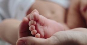 A close-up of a baby's foot resting gently in an adult's hand, with the baby's soft skin and tiny toes in focus.