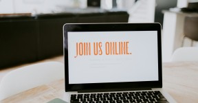 A laptop on a table with the words join us online on the screen. in orange writing.