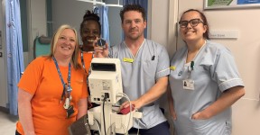 Hospital staff standing beside clinical monitoring equipment in a hospital ward.