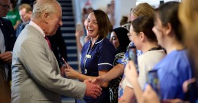 His Majest King Charles shaking hands with a member of the public while surrounded by other healthcare professionals.