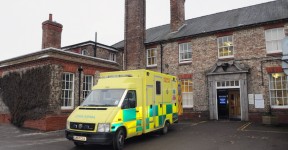 An ambulance parked outside an entrance to an old hospital building.