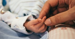 An adult's hand touching the hand of a newborn baby.