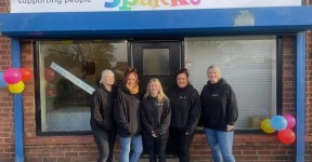Five people standing outside the Sparks premises, beneath a colourful sign reading “Sparks – supporting people and communities”. Colourful balloons decorate the front of the building.
