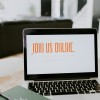 A laptop on a table with the words join us online on the screen. in orange writing.