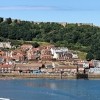 Panoramic view of Scarborough seafront with the harbour, sandy beach, and Scarborough Castle on the green headland overlooking the town.