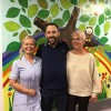 Jamie with neo-natal support worker Anita Brown and his mum June. A mural of a tree is on the wall behind them.