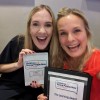 Two smiling women holding up a sign and a certificate.