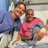 Research Midwife Marie Home posing with new mum Danielle Woodward and her baby son Leif. Danielle is sitting in a hospital bed, holding Leif, while Marie stands alongside them in her work scrubs.