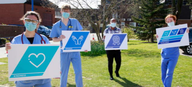 Three Junior Doctors and clinical lead Ru outside at Scarborough Hospital holding large signs with the new Trust Values on for Kindness, Openness and Excellence