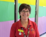 A person wearing glasses and a red shirt, smiling in front of a colourful rainbow background.