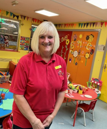 Tracey wearing her Play Team uniform (a red polo shirt) in a playroom.