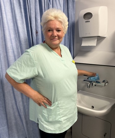 Jane smiling at work while cleaning a sink in a hospital room.