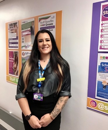 Annabel in front of a Staff Benefits wall display down a hospital corridor.