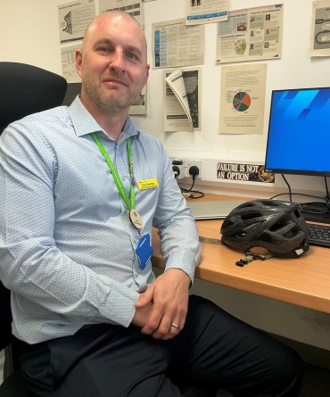 Dan alongside his desk. There is a cycling helmet on top of the desk.