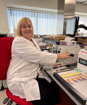 Natalie at work using lab equipment and wearing a white lab coat.