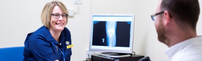 Member of staff speaking to a patient besides a computer screen showing X-ray results.