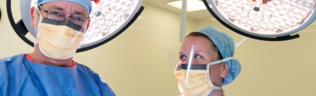 Two members of staff in an operating theatre, both wearing PPE.