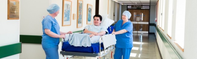 Banner image featuring a patient in a bed being wheeled by two surgical members of staff.
