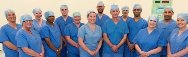 Banner image featuring 14 members of staff standing together, all wearing blue scrubs and surgical caps.