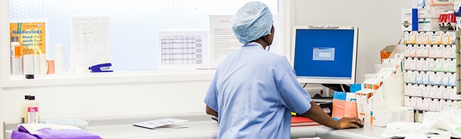 A nurse in scrubs in a medical room using a computer