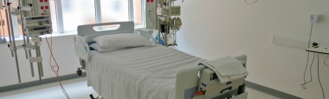 An empty critical care bay with a bed and monitors in a light room