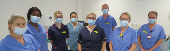 A group of eight endoscopy staff in blue nursing uniforms and blue scrubs lined up in a patient rest room.