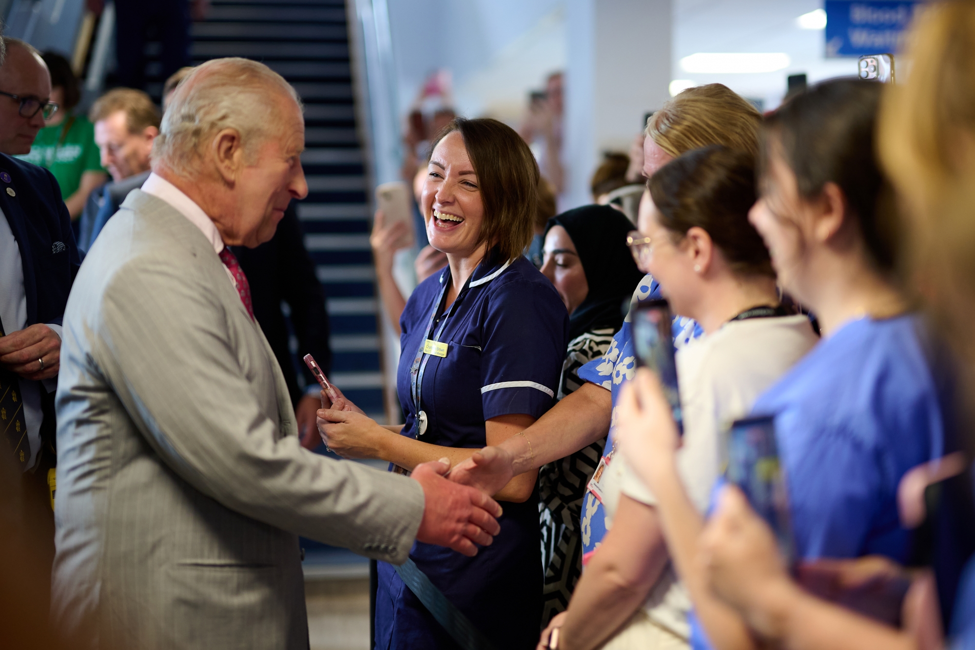 His Majest King Charles shaking hands with a member of the public while surrounded by other healthcare professionals.