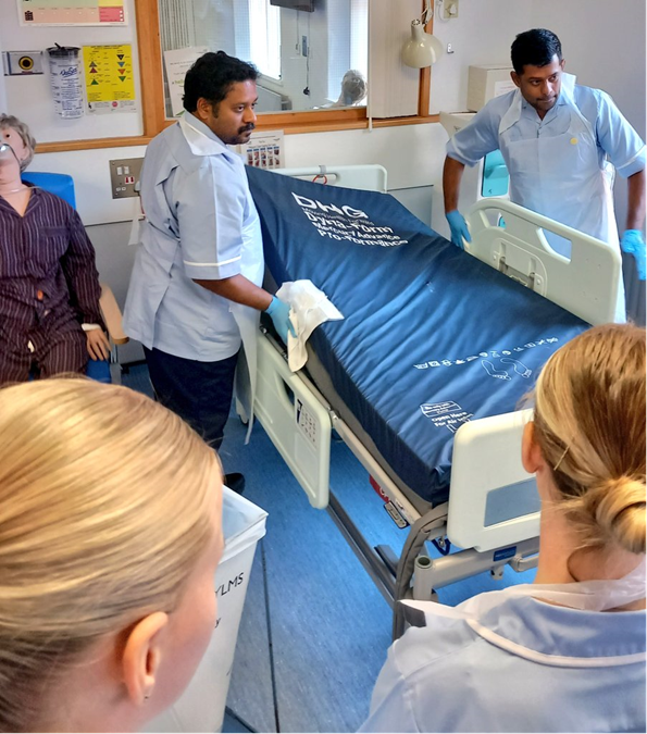 Two staff members undergoing training with an empty hospital bed.