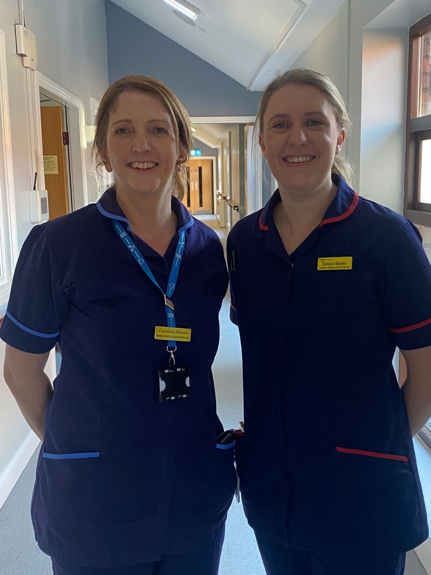 Caroline and Debbie, palliative nurses at the Trust, standing on a hospital corridor in their work uniforms.